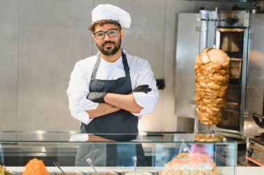 Lokantasında çapraz kollarla poz veren Ortadoğu şefi shawarma rosto ve taze malzemelerini gururla sergiliyor.