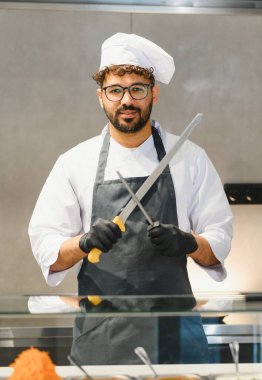 Orta Doğulu şef siyah eldiven ve önlük takarak büyük bıçağı biliyor, profesyonel restoran mutfağında lezzetli kebap ya da shawarma yapmaya hazırlanıyor.