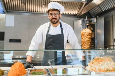 Orta Doğulu aşçı üniforma ve önlük giyip fast food restoranında çalışıyor, lezzetli shawarma ve diğer geleneksel yemekleri hazırlıyor.
