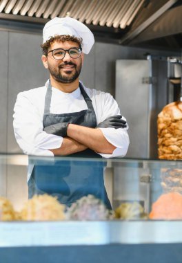 Siyah eldiven ve önlük takan kendine güvenen şef yemek kamyonunda gülümsüyor ve ön planda shawarma ve diğer doğu yemekleri var.