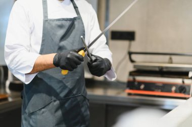 Profesyonel aşçı bıçağını çelik bileyiciyle biler, ticari mutfakta yemek hazırlamaya hazırlanır.