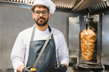 Profesyonel aşçı bıçakları ustalıkla tutarken ağız sulandırıcı shawarma 'yı hareketli bir ticari mutfak ortamında hazırlıyor.