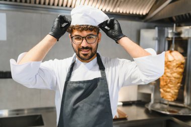 Gülümseyen aşçı şef şapkasını düzeltiyor, profesyonel bir mutfakta lezzetli shawarma ya da kebap yapmaya hazırlanıyor.