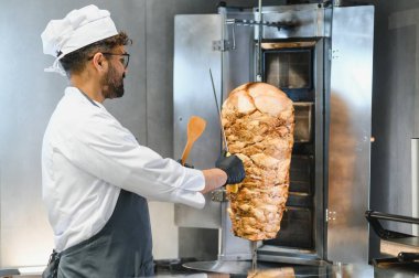 Profesyonel bir aşçı dikey bir restorandan ustalıkla kızarmış et dilimliyor. Ticari bir mutfakta leziz bir shawarma hazırlıyor.
