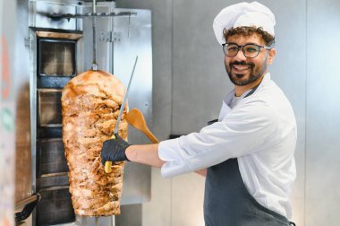 Büyük bir bıçak ve ahşap bir spatula kullanarak et doğrayan gülümseyen bir şef.