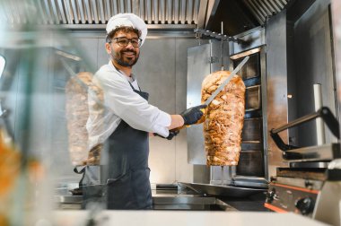 Pişirmek uzun bıçak kullanarak lezzetli tavuk shawarma hazırlamak, profesyonel mutfakta orta doğu mutfağı sanatını sergilemek