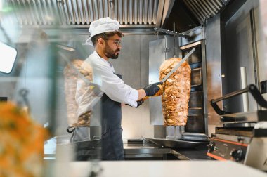 Profesyonel bir aşçı, geleneksel bir orta doğu yemeği hazırlamak için ticari bir mutfakta döner tükürükten shawarma eti dilimlemek için uzun bıçaklar kullanır.