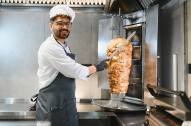 Profesyonel şef modern bir yemek kamyonunun mutfağında lezzetli shawarma etini ustalıkla dilimliyor ve popüler bir sokak yemeği hazırlıyor.