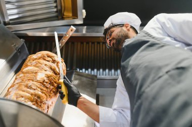 Profesyonel bir aşçı, ticari bir mutfakta baharatlı shawarma etini dönüşümlü bir tükürükten ustalıkla doğruyor ve popüler bir sokak yemeği hazırlıyor.