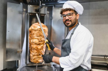 Profesyonel şef dikey bir et lokantasından taze eti ustalıkla dilimliyor, bir restoranın mutfağında ağız sulandıran bir shawarma yapıyor.