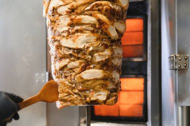 Bir fast food restoranında lezzetli kızarmış shawarma hazırlarken ahşap bir spatula tutarak yemek pişirmek ağız sulandıran aromalar yaratıyor.