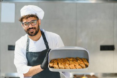 Siyah eldiven giyen profesyonel aşçı ve önlük taşıyan baklava hamur işleri, Orta Doğu veya Akdeniz mutfağında uzmanlık gösteriyor