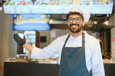 Mutlu aşçı siyah eldiven giyer ve fast food restoranının menüsünü gösterir.