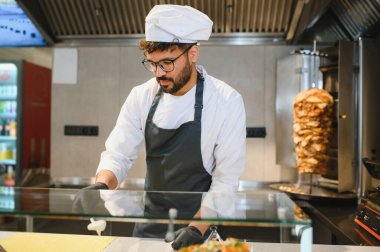 Orta Doğulu şef, kalabalık bir lokantada taze malzemeler kullanarak bir donör kebabı hazırlıyor.
