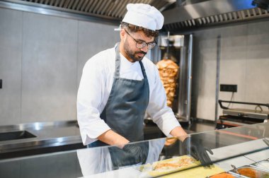 Profesyonel aşçı siyah eldiven takıyor. Swawarma ya da kebabı dikkatlice hazırlıyor. Hijyenik ticari bir mutfakta taze malzemeler kullanıyor.