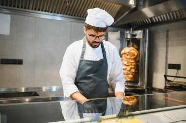 Siyah eldiven ve önlük takan aşçı bir lokantada kebap ya da shawarma hazırlıyor.
