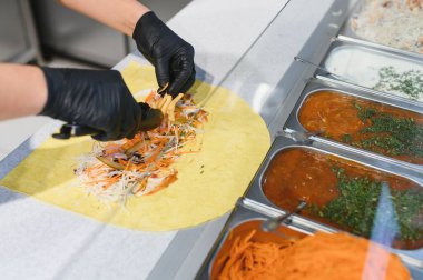 Et ve sebzeli bir shawarmaya patates kızartması ekleyen aşçı, yanında da soslu ve doğranmış havuç.