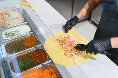 Lavaş ya da pita ekmeğine doğranmış sebze, çeşitli soslar ve malzemelerle metal kaplarda görünür.