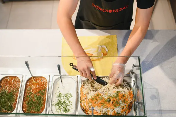 Donör kebabı pişir, sandviçe metal maşayla taze salata ekle, metal kaplarda soslar olsun.