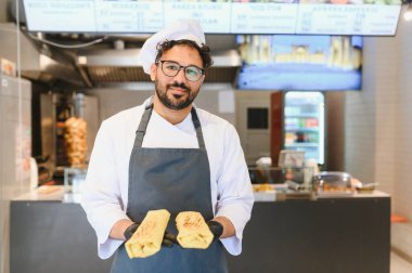 Siyah eldiven giyen Arap şef bir fast food restoranında iki yeni yapılmış shawarma tutuyor.