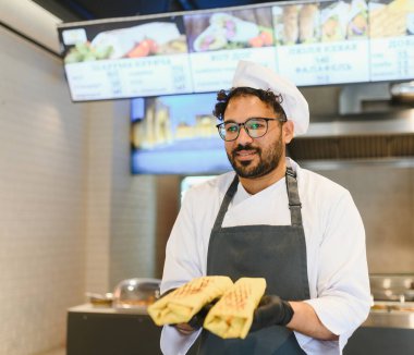 Kendine güvenen şef elinde iki lezzetli shawarma gösteriyor, doğu mutfağında uzmanlaşmış bir fast food restoranında çalışıyor.
