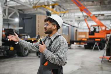 Güvenlik kaskı takan Arap mühendis modüler bir ev üretim tesisinde telsiz konuşmaları düzenliyor.