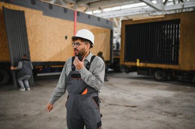 Arap inşaat işçisi güvenlik kaskı takıyor ve telsiz kullanıyor. Modüler bir ev üretim tesisinde yapılan operasyonların koordinatları.