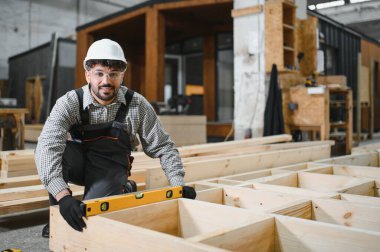 Atölye ortamında prefabrik modüler ev bölümünün yapımında hassasiyet sağlamak için ruh seviyesini kullanan yetenekli bir marangoz.