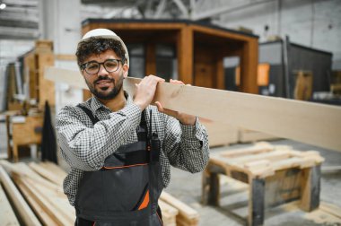 Ahşap kalas taşıyan marangoz, yoğun atölyede prefabrik ev projesi üzerinde çalışıyor, modüler inşaatlarda uzmanlık ve kendini adamışlık gösteriyor.