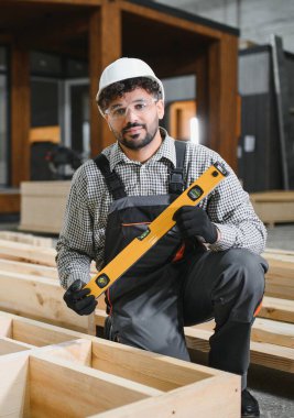 Orta Doğulu marangoz marangozluk atölyesinde prefabrik ev yapısı üzerinde çalışırken ruh seviyesini kullanıyor.