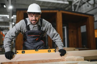 Marangoz, prefabrik ev inşaatında ahşap seviyeyi ruh seviyesiyle kontrol ediyor.