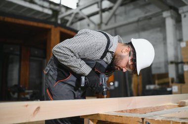 Parlak bir atölyede modüler ev inşaatı için kablosuz matkap ve ahşap çerçeve kullanarak odaklanmış marangoz.