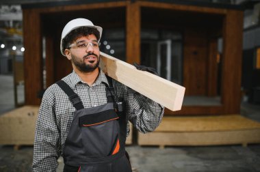Arap inşaat işçisi, omuzunda ahşap tahta taşıyor prefabrik ev fabrikasında çalışıyor.