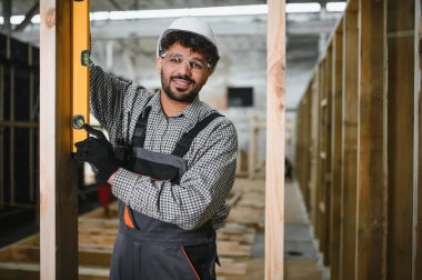 Arap inşaat işçisi prefabrik ev atölyesindeki ruh seviyesini kullanarak ahşap kirişin dikeyliğini kontrol ediyor.