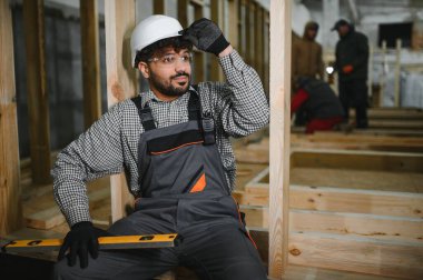 İnşaat atölyesinde çalışan bir işçi modüler bir ev inşa ediyor. Hassasiyet ve işçiliğe odaklanmış, araçlar ve uzmanlık