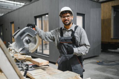 Modern bir atölye ortamında marangozluk alanında uzmanlık ve hassasiyet gösteren dairesel bir testere kullanırken usta bir marangoz başparmak kaldırıyor.