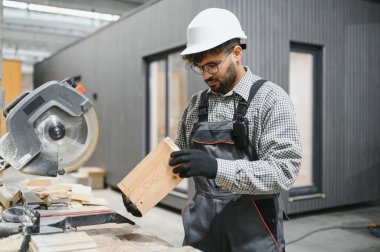 Yetenekli bir marangoz, ahşap bir kalası inceliyor, prefabrik bir ev üretim tesisinde çalışmaya hazırlanıyor.