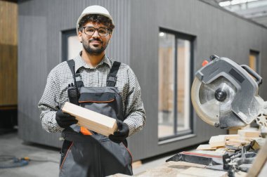 Usta marangoz ahşap kalası inceliyor, prefabrik ev atölyesinde inşaata hazırlanıyor, modüler yapı konusunda uzmanlık gösteriyor.