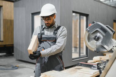 Marangoz titizlikle ahşap kalasları inceliyor, prefabrik modüler ev yapımında kaliteyi sağlıyor, modern yapı tekniklerinde uzmanlık ve hassasiyet gösteriyor.