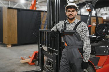 Arap forklift operatörü modüler ev fabrikasında makinesine yaslanıyor.