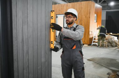 Arap inşaat işçisi prefabrikasyon atölyesinde ruh seviyesini kullanarak modüler duvar panelinin dikeyliğini kontrol ediyor