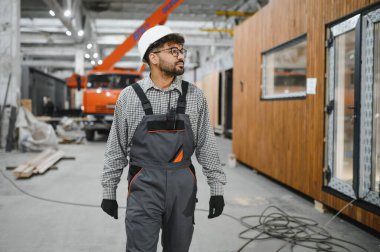 Arap inşaat işçisi büyük endüstriyel atölye içinde prefabrik modüler ev bölümünde yürüyor ve teftiş ediyor