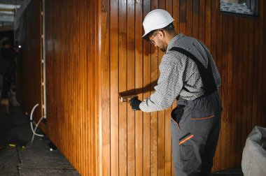 Prefabrik modüler ev yapım atölyesinin ahşap duvar bölümüne vernik uygulayan yetenekli bir işçi.