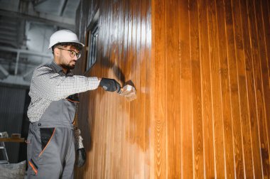 Modüler ev üretiminde ahşap duvara vernik uygulayan yetenekli işçiler, inşaat atölyesinde kalite ve koruma sağlıyorlar.