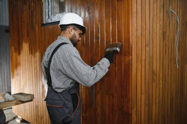 Ahşap panellere vernik uygulayan yetenekli işçiler, bir inşaat atölyesinde modüler ev üretimine katkıda bulunuyorlar.