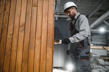 İnşaat atölyesindeki prefabrik modüler ev için ahşap döşemeleri cilalayan odaklı marangoz.