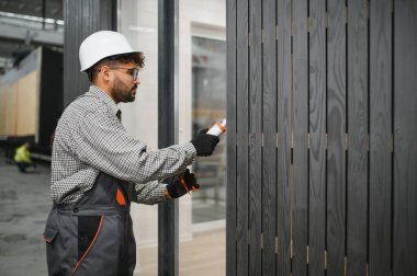 Yetenekli inşaat işçisi prefabrik modüler bir evin dış duvarına dolgu macunu sürerek modern bir fabrika ortamında hava direnci ve dayanıklılık sağlar.