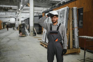 Arap inşaat işçisi modüler ev üretim fabrikasında dikilirken kaskını düzeltiyor.