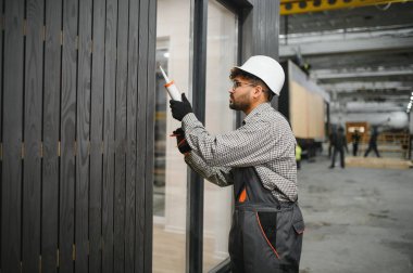 İnşaat işçisi fabrikada prefabrik modüler ev bölümünün eklemlerine dolgu macunu sürüyor.