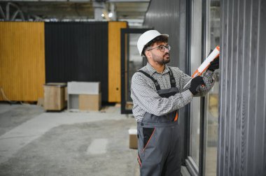 Fabrika ortamında prefabrik modüler bir evin dış yüzeyine dolgu macunu süren yetenekli bir inşaat işçisi.